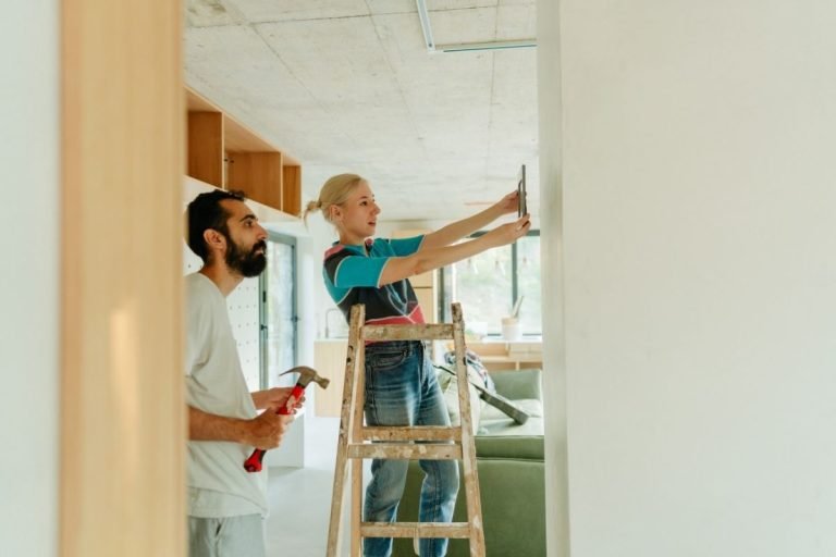 A man and woman are painting a room together, with brushes and paint cans, focused on their task.